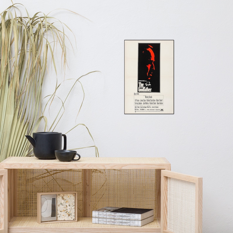 May include: A vintage movie poster for the film "The Godfather" featuring a red silhouette of Marlon Brando's face. The poster has a black border and white background.