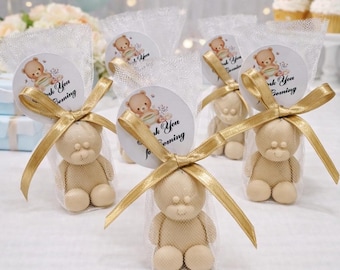 May include: A set of party favors featuring small beige teddy bear figurines inside clear mesh bags. Each bag is tied with a gold ribbon and includes a round white tag with a teddy bear illustration and the text Thank You for Coming.