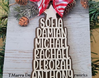 May include: A Christmas tree-shaped ornament with names cut out in a layered design. The ornament is topped with a red and white striped bow and a red berry. The names Sofia, Damian, Michael, Rachael, Deborah, Anthony, and Gabrielle are visible.