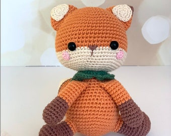 May include: A crocheted fox plush toy with orange fur, brown legs, and a green scarf. The fox has black eyes and pink cheeks.