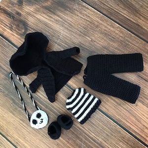 K&ouml;nnte beinhalten: Ein schwarzes H&auml;kel-Outfit f&uuml;r eine Puppe, bestehend aus einer Kapuzenjacke, einer Hose, einer gestreiften M&uuml;tze, einer kleinen Tasche mit einem Pandagesicht und Schuhen.