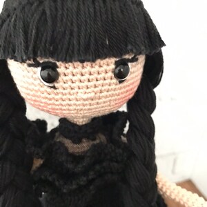 May include: A crocheted doll with black hair, a black dress, and black eyes.