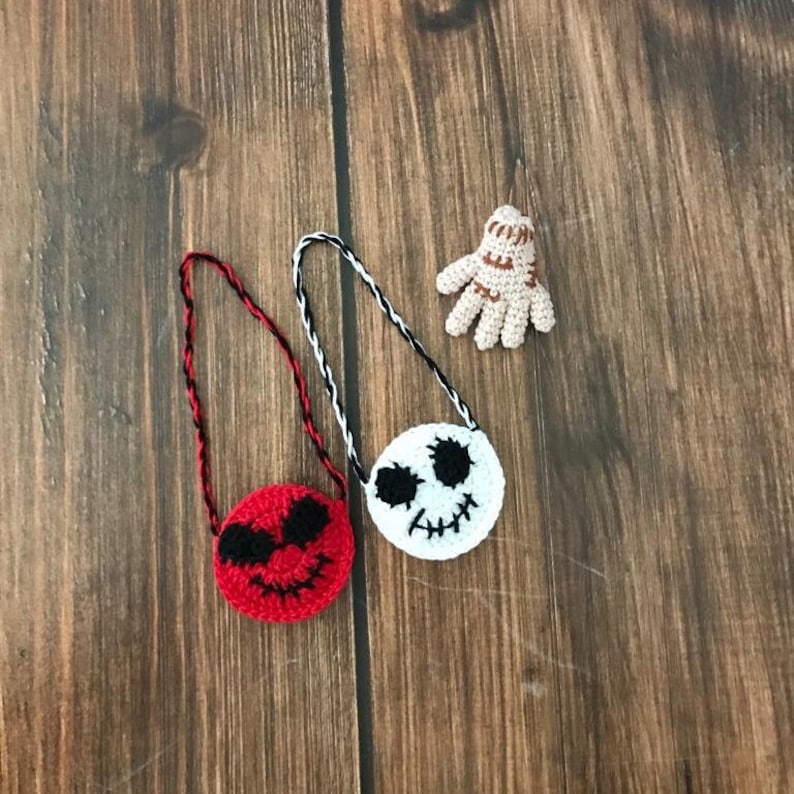 May include: Two small crocheted purses with character faces. One is red with black eyes and a smile, the other is white with black eyes and a stitched mouth. Both have black and white cords.