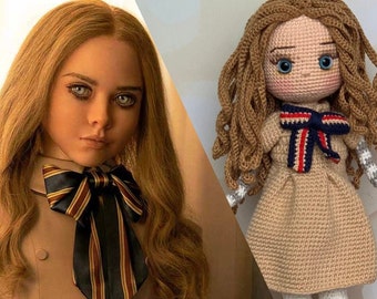 Könnte beinhalten: Eine gehäkelte Puppe mit langen braunen Haaren, die ein beiges Kleid mit einer rot-weiß-blauen gestreiften Schleife trägt. Die Puppe hat blaue Augen und ein gehäkeltes Gesicht.