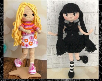 May include: Two crocheted dolls, one with blonde hair wearing a pink and orange striped shirt and a white skirt with pink flowers, and the other with black hair wearing a black dress with a black lace overlay and white and black striped socks.