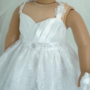 May include: White lace and satin dress with a beaded belt and straps. The dress is designed for a doll and has a full skirt.