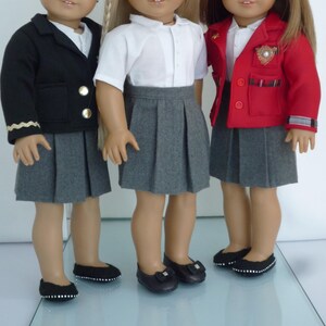 May include: Three dolls wearing school uniforms. One doll is wearing a black blazer with gold buttons, a white shirt, and a gray pleated skirt. Another doll is wearing a white shirt, gray pleated skirt, and black shoes. The third doll is wearing a red blazer, white shirt, gray pleated skirt, and black shoes.