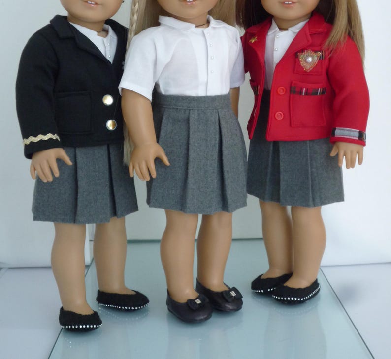 May include: Three dolls wearing school uniforms. One doll is wearing a black blazer with gold buttons, a white shirt, and a gray pleated skirt. Another doll is wearing a white shirt, gray pleated skirt, and black shoes. The third doll is wearing a red blazer, white shirt, gray pleated skirt, and black shoes.