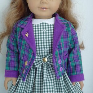 May include: A doll wearing a green and purple plaid jacket with a purple collar and a green and white gingham dress.