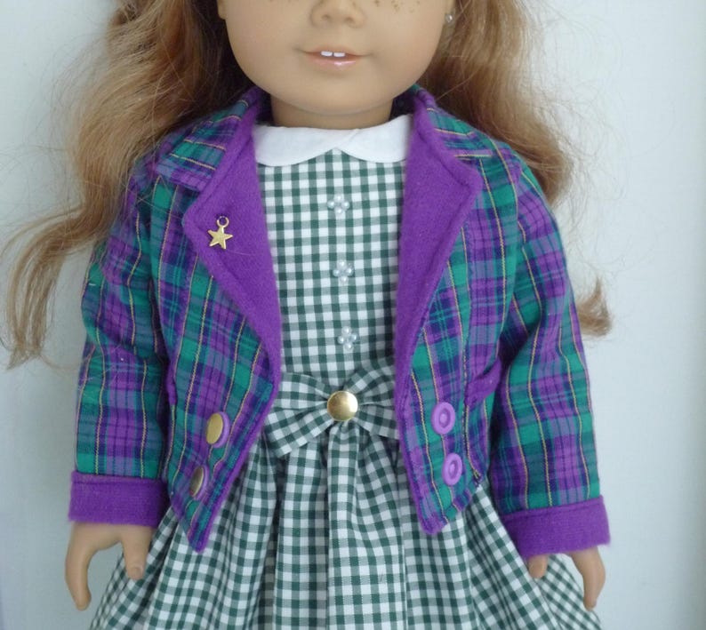 May include: A doll wearing a green and purple plaid jacket with a purple collar and a green and white gingham dress.