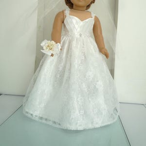 May include: White lace wedding dress with a satin bodice and a flower bouquet for a doll.