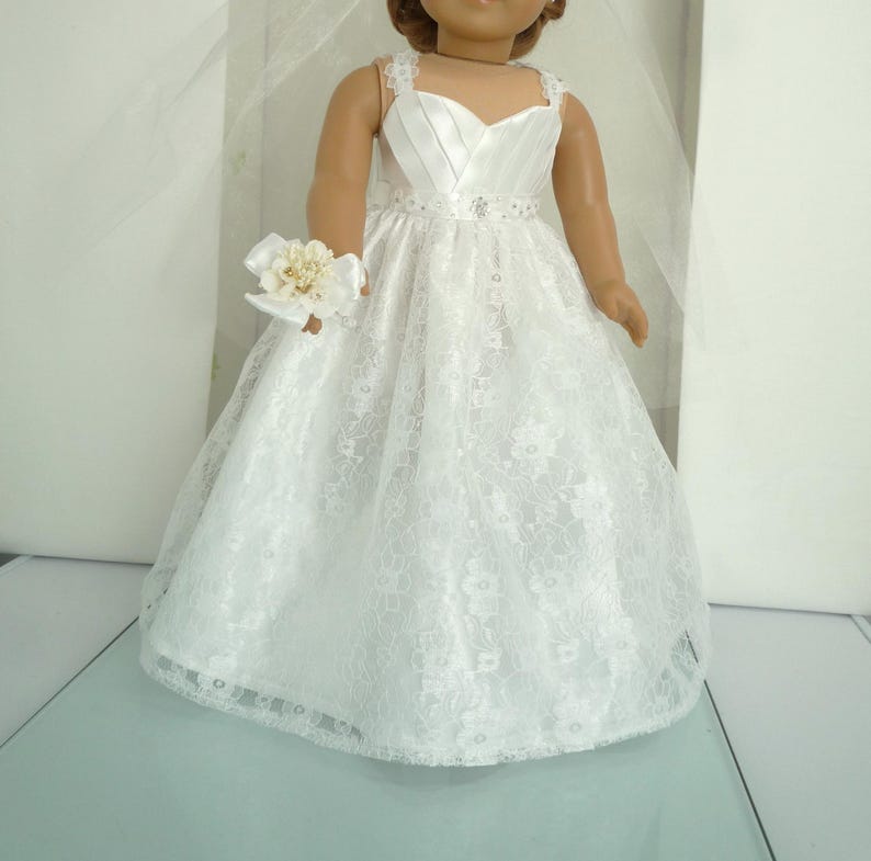 May include: White lace wedding dress with a satin bodice and a flower bouquet for a doll.