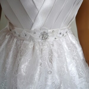 May include: White satin bodice with a lace skirt and a rhinestone embellishment on the waist.