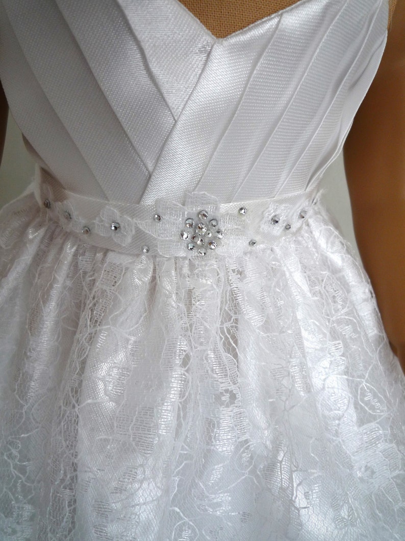 May include: White satin bodice with a lace skirt and a rhinestone embellishment on the waist.