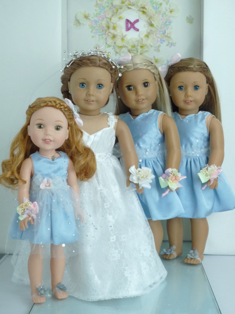 May include: Four dolls dressed in blue and white dresses. The doll in the center is wearing a white lace dress with a silver tiara. The other three dolls are wearing light blue dresses with floral embellishments.