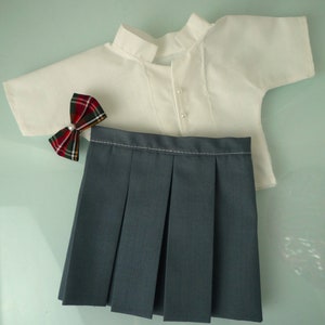 May include: A doll-sized school uniform set, featuring a white short-sleeved shirt with pearl buttons, a pleated gray skirt, and a plaid bow tie with a pearl center. The outfit is designed for a doll.