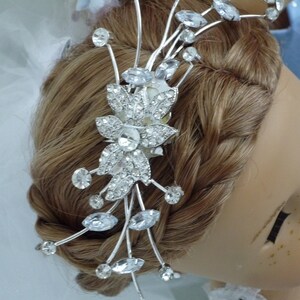 May include: A silver bridal hair comb with a floral design and crystal accents. The comb is placed in a woman's brown hair.