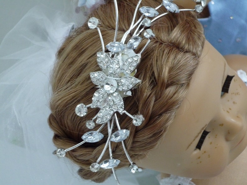 May include: A silver bridal hair comb with a floral design and crystal accents. The comb is placed in a woman's brown hair.