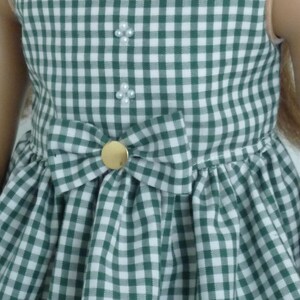 May include: A green and white gingham dress with a white collar and a bow at the waist. The dress has three pearl-like buttons down the front.
