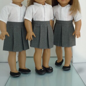 May include: Three dolls dressed in school uniforms. Each doll wears a white collared shirt, a gray pleated skirt, and black shoes. The dolls are standing side by side, showcasing the uniform's design and fit.