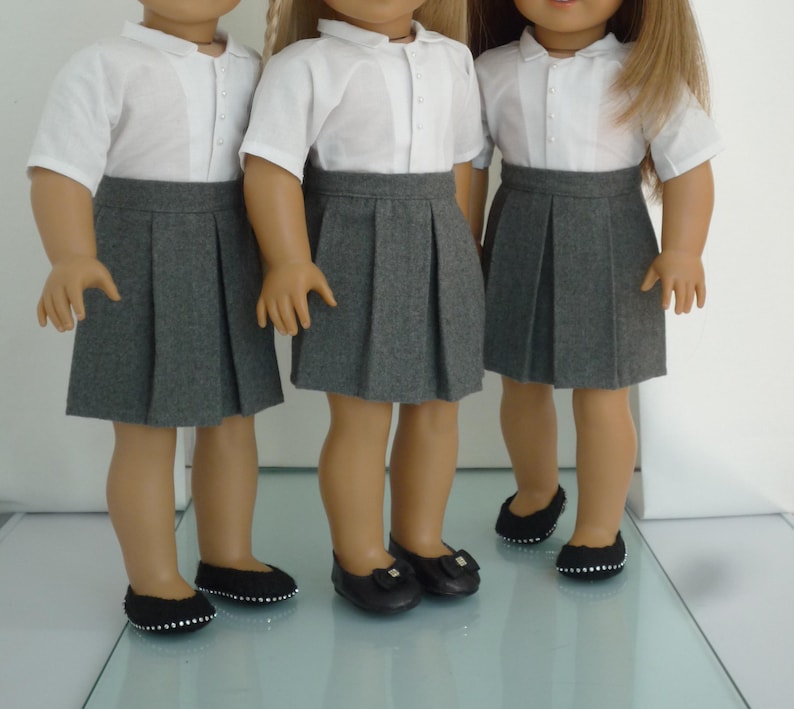 May include: Three dolls dressed in school uniforms. Each doll wears a white collared shirt, a gray pleated skirt, and black shoes. The dolls are standing side by side, showcasing the uniform's design and fit.
