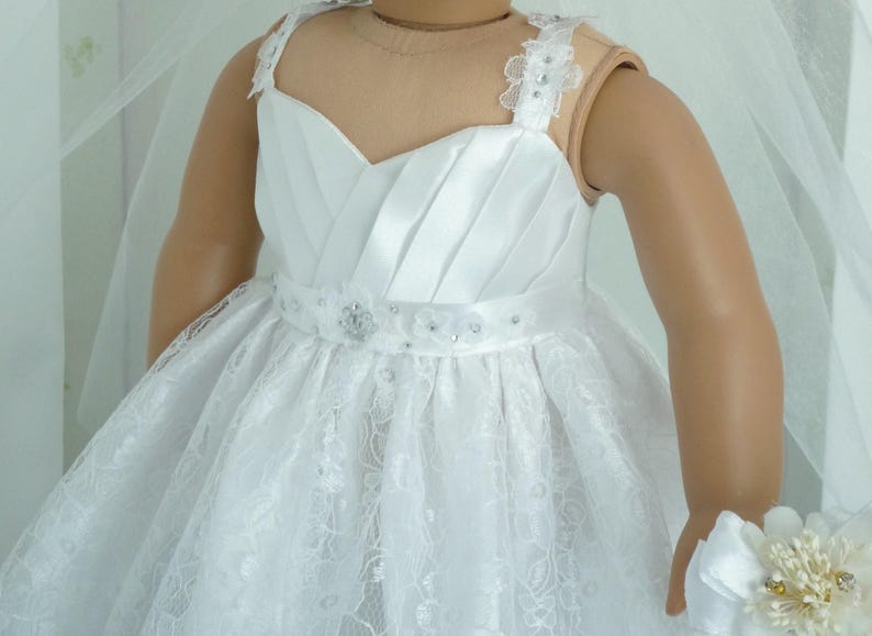 May include: White lace and satin dress with a beaded belt and straps. The dress is designed for a doll and has a full skirt.