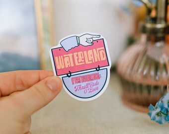 May include: A pink and orange sticker with the text "Waterland" and a hand pointing to the right. The sticker also has the text "Featuring: Thrill Ride O' Love" in a white bowl.