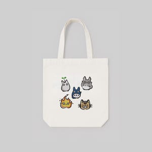 May include: A white tote bag with a design featuring cartoon characters. The bag has a rectangular shape and two handles. The cartoon characters are in various colours and shapes, including a blue creature and a cat-like character.