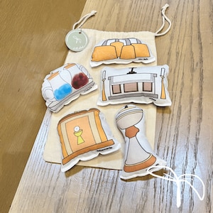 May include: A set of felt religious items for children. The set includes a tabernacle, an altar, a chalice, a ciborium, and two cruets. The items are all white with black outlines and have various details like a cross, a chalice, and a ciborium.
