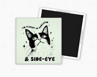 May include: A square magnet with a black and white cat illustration. The cat has a sassy expression and the text reads "I'M FLUENT IN SARCASM & SIDE-EYE". A second black magnet is visible in the background.