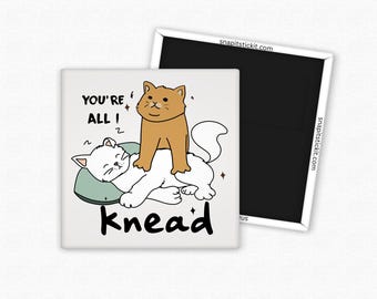 May include: Square magnet with a cartoon illustration of two cats. One cat is lying down on a pillow, and another cat is sitting on top of it. The text "YOU'RE ALL ! knead" is written on the magnet.
