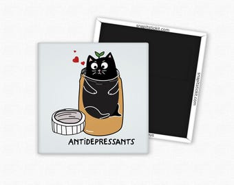 May include: A square magnet with a cartoon illustration of a black cat inside a jar labeled "ANTIDEPRESSANTS". The cat has a green sprout on its head and is surrounded by red hearts. A separate magnet is visible in the background.