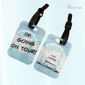 May include: Two rectangular luggage tags with black adjustable straps. One tag features the text I'M GOING ON TOUR! in black letters. The other tag displays the text NAME: LIANNE, DESTINATION: INTO THE MILLENNIUM, with a group photo background.