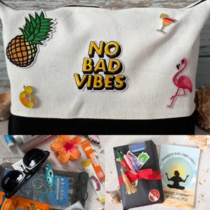 May include: A white canvas tote bag with a black base, adorned with embroidered patches including a pineapple, a flamingo, and the text "NO BAD VIBES". The bag is filled with sunglasses, a journal, and other beach-themed accessories.