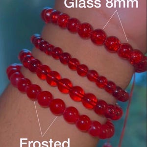 May include: Four red beaded bracelets made of 8mm glass beads. Two bracelets feature a cracked glass texture, while the other two consist of frosted glass beads. Each bracelet is strung on a thin cord, displaying a uniform round bead design.