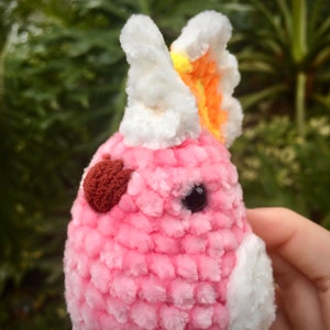 Op de afbeelding: Een roze gehaakt pluche speelgoed met een witte en oranje gehaakte vlinder erop. Het speelgoed heeft een bruine hartvormige neus en zwarte ogen.
