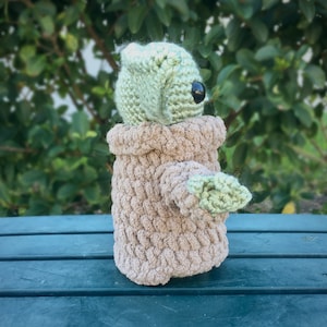 Puede incluir: Mu&ntilde;eco de ganchillo hecho a mano a semejanza de un personaje popular. El mu&ntilde;eco tiene una cabeza verde claro con grandes ojos negros y un cuerpo de color canela. El mu&ntilde;eco est&aacute; hecho de hilo suave y texturizado y tiene brazos peque&ntilde;os.