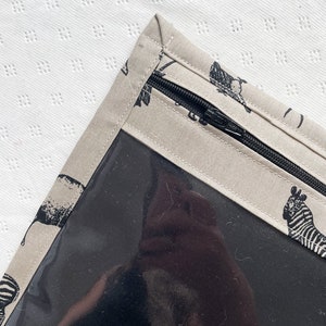 May include: A beige fabric zippered pouch with a clear plastic window. The pouch has a black zipper and a black and white animal print design.