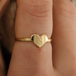 May include: A gold heart-shaped ring with the letter "S" engraved on the front.