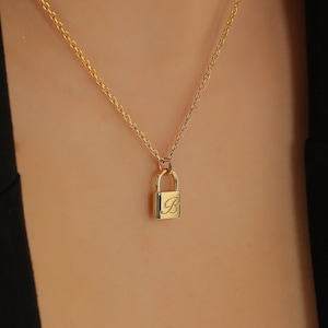May include: A gold chain necklace with a small padlock pendant engraved with the letter "B".