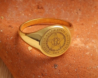May include: A gold signet ring with a circular design featuring the words "Stephen F. Austin State University" and the year "1923".