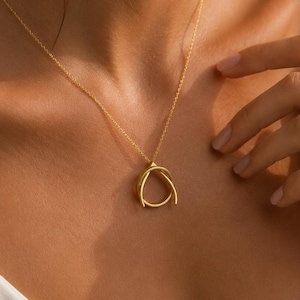 May include: A gold-toned necklace featuring a delicate chain and a pendant composed of two interlocking, smooth, curved metal loops that form a rounded, abstract shape resting against the collarbone area of the neck.