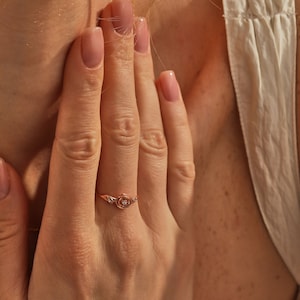 May include: A rose gold ring with a small diamond in the center of a rose design.