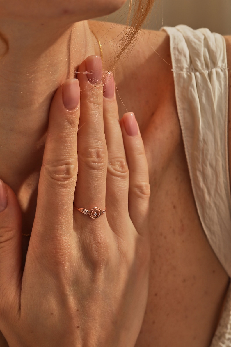May include: A rose gold ring with a small diamond in the center of a rose design.