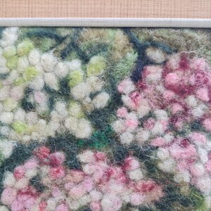 May include: A framed textile artwork depicting a close-up of a floral design. The piece features white, pink, and green hues, with a textured, felted appearance. The frame is a light grey colour.