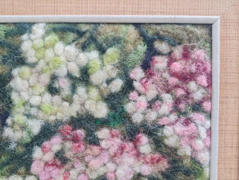 May include: A framed textile artwork depicting a close-up of a floral design. The piece features white, pink, and green hues, with a textured, felted appearance. The frame is a light grey colour.