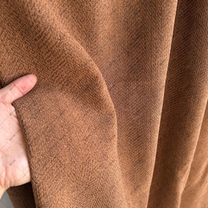 Puede incluir: Primer plano de una tela marrón con un sutil patrón de espiga. La tela tiene un tacto suave y texturizado.