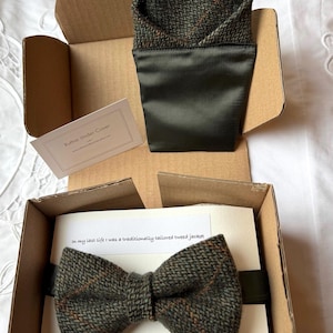 Może przedstawiać: Zestaw muszki i poszetki z tweedu w kartonowym pudełku. Muszka i poszetka są zielone, brązowe i pomarańczowe. Poszetka jest złożona i umieszczona w ciemnozielonej satynowej kieszeni. W zestawie karta z tekstem.