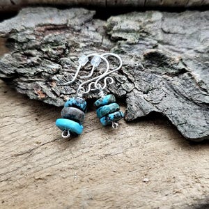 May include: A pair of silver earrings with turquoise stones. The stones are stacked on top of each other and have a mottled blue and black pattern.