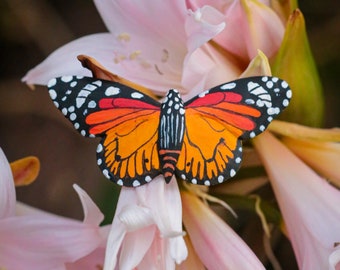 May include: A close-up of a colorful butterfly with black, orange, and white wings, perched on a pink flower.